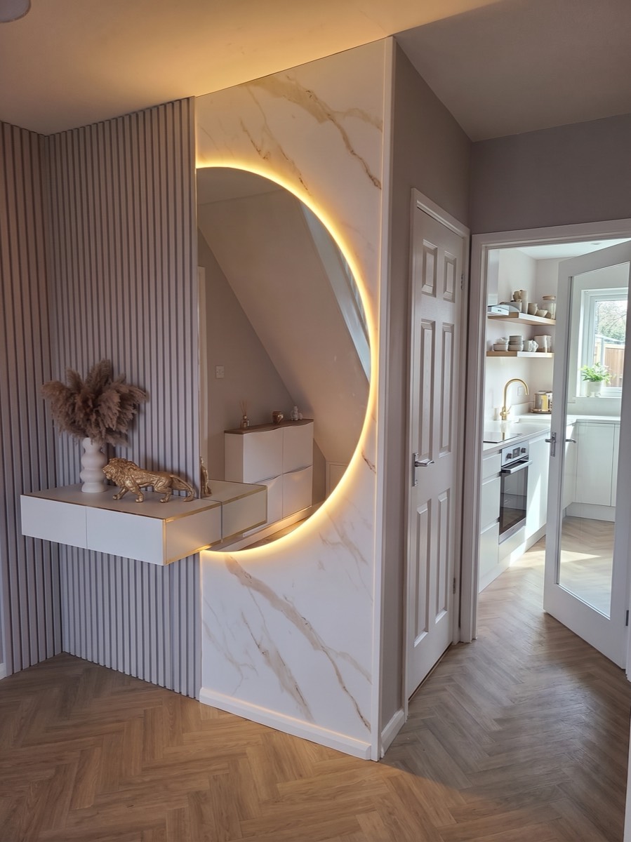 A backlit mirror set into a gold-veined marble feature panel beside a fluted slat wall