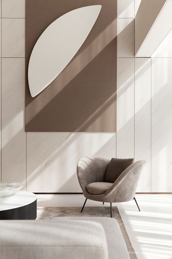 A pale stone-panelled living room wall with a taupe fabric panel and a grey velvet armchair in raking light